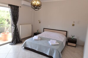 A bedroom with a bed, a radiator, a potted plant, a nightstand, and a wall-mounted light fixture. - CHALKIDA PEARL (Xirovrisi)