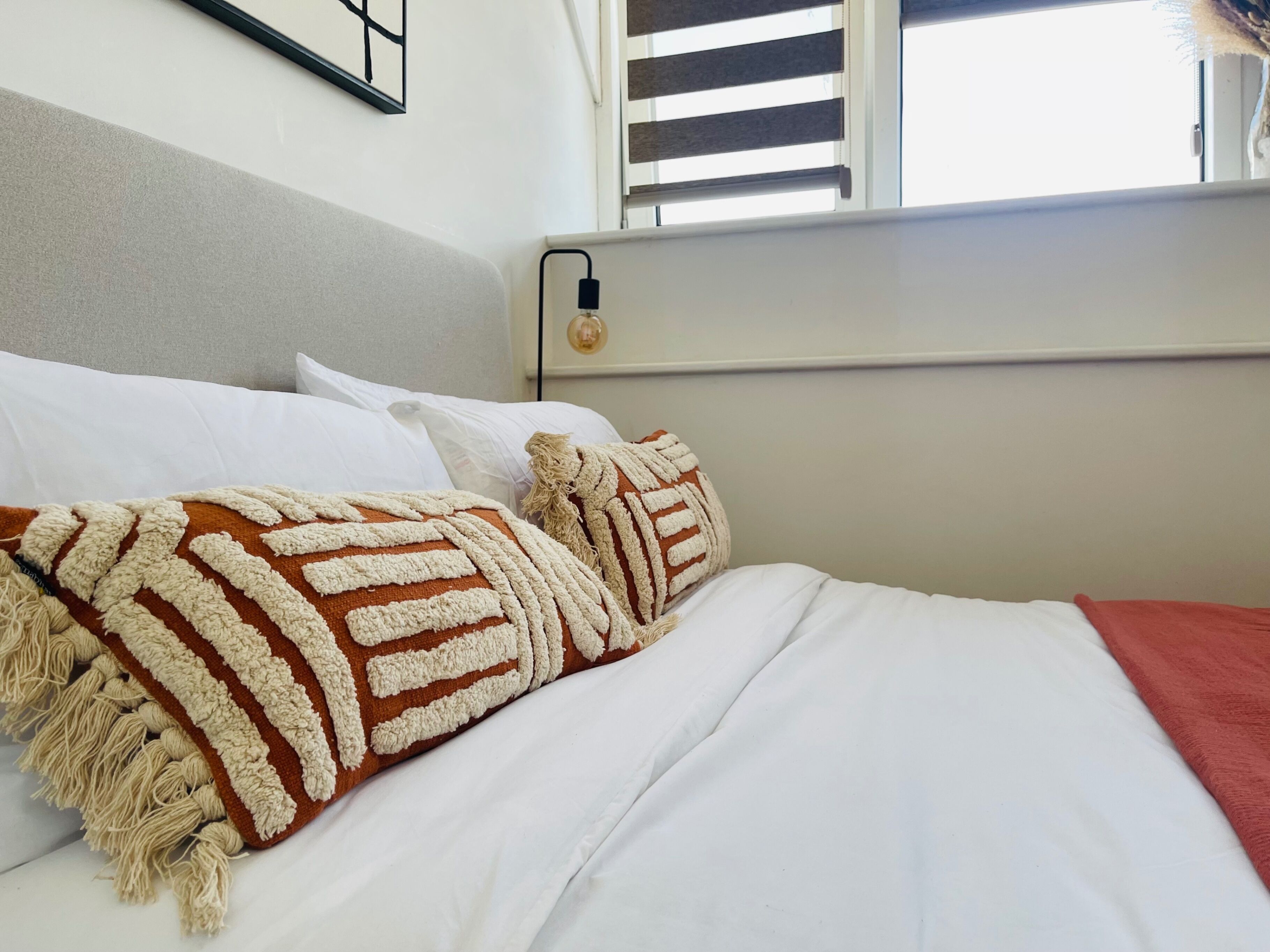 A bed with white bedding, a brown and white striped throw blanket, and a red blanket.