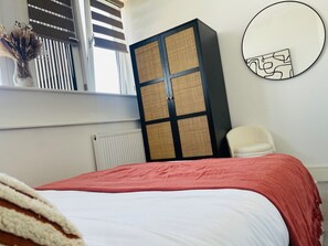 A bedroom with a bed, a radiator, a window with blinds, a chair, and a wall-mounted mirror.