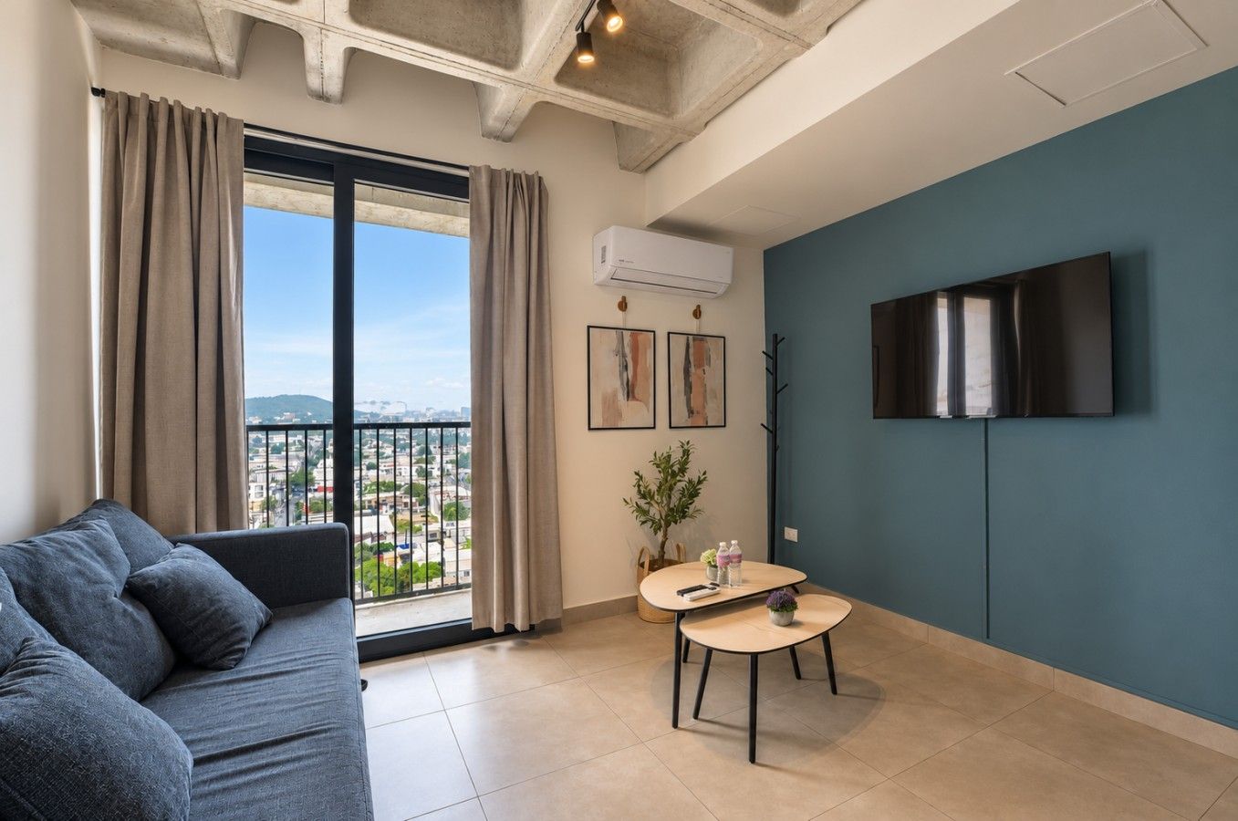 A modern living room with a sofa, a small table, a TV, and a balcony with curtains.