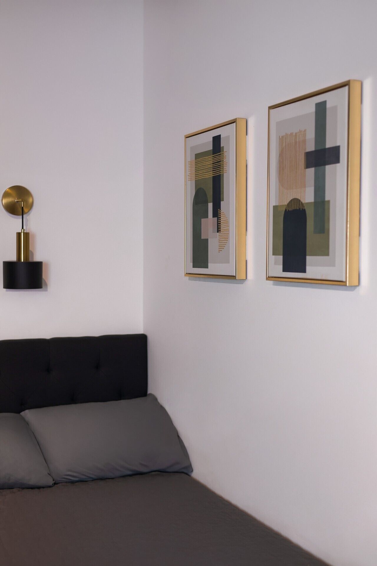 A bedroom with a bed, two framed abstract paintings, and a wall-mounted lamp.