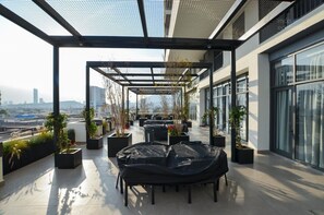 A rooftop terrace with outdoor seating, potted plants, and a city view.