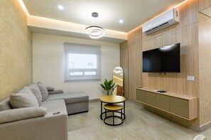 A modern living room with a sofa, a small round table, a TV mounted on a wooden wall, and an air conditioning unit. - ¡Céntrico & Nuevo! Gym, Parking & Pool - 6G 2BR2br (Monterrey)