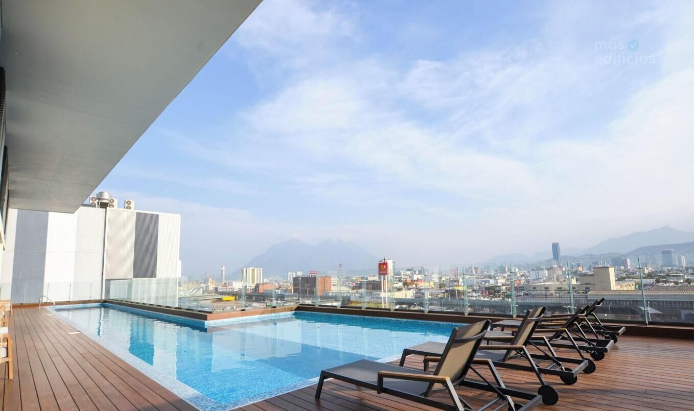 A rooftop pool with lounge chairs and a cityscape view.