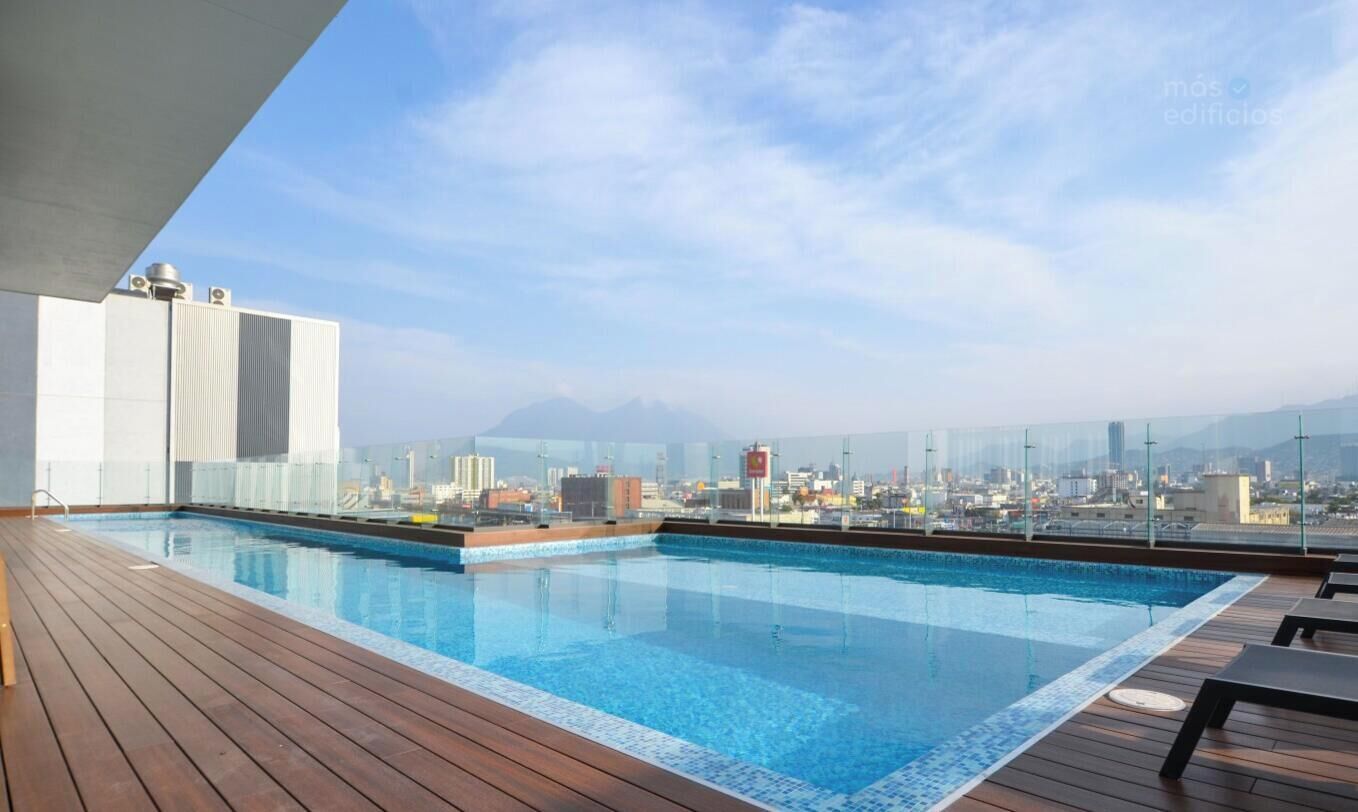 A rooftop pool with a city view, wooden deck, and a glass barrier.