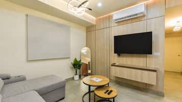 A modern living room with a sofa, a round table, a TV mounted on a wooden wall, and an air conditioning unit.