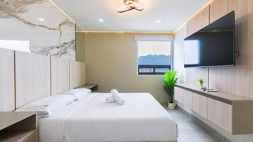 A modern hotel room with a bed, a flat-screen TV, a window with a view, and a plant.