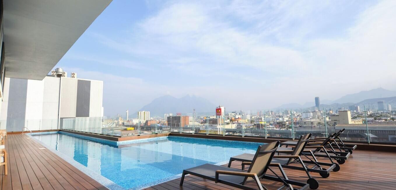 A rooftop pool with lounge chairs and a city view.
