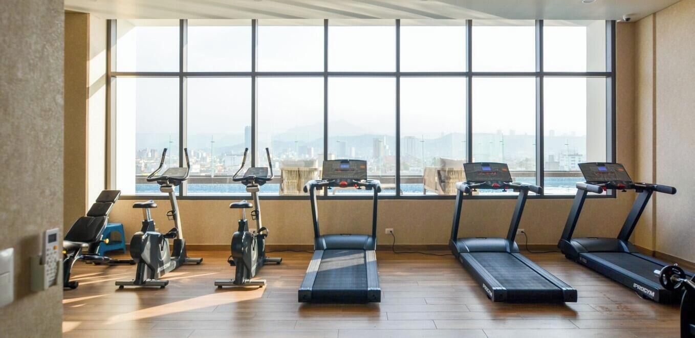 A gym with exercise equipment and a large window overlooking a cityscape.