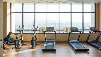A gym with exercise equipment and a large window overlooking a cityscape.