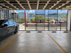 Een parkeergarage met een auto op een geëtiketteerde plek, betonnen muren en een uitzicht op een bergachtig landschap door grote ramen.