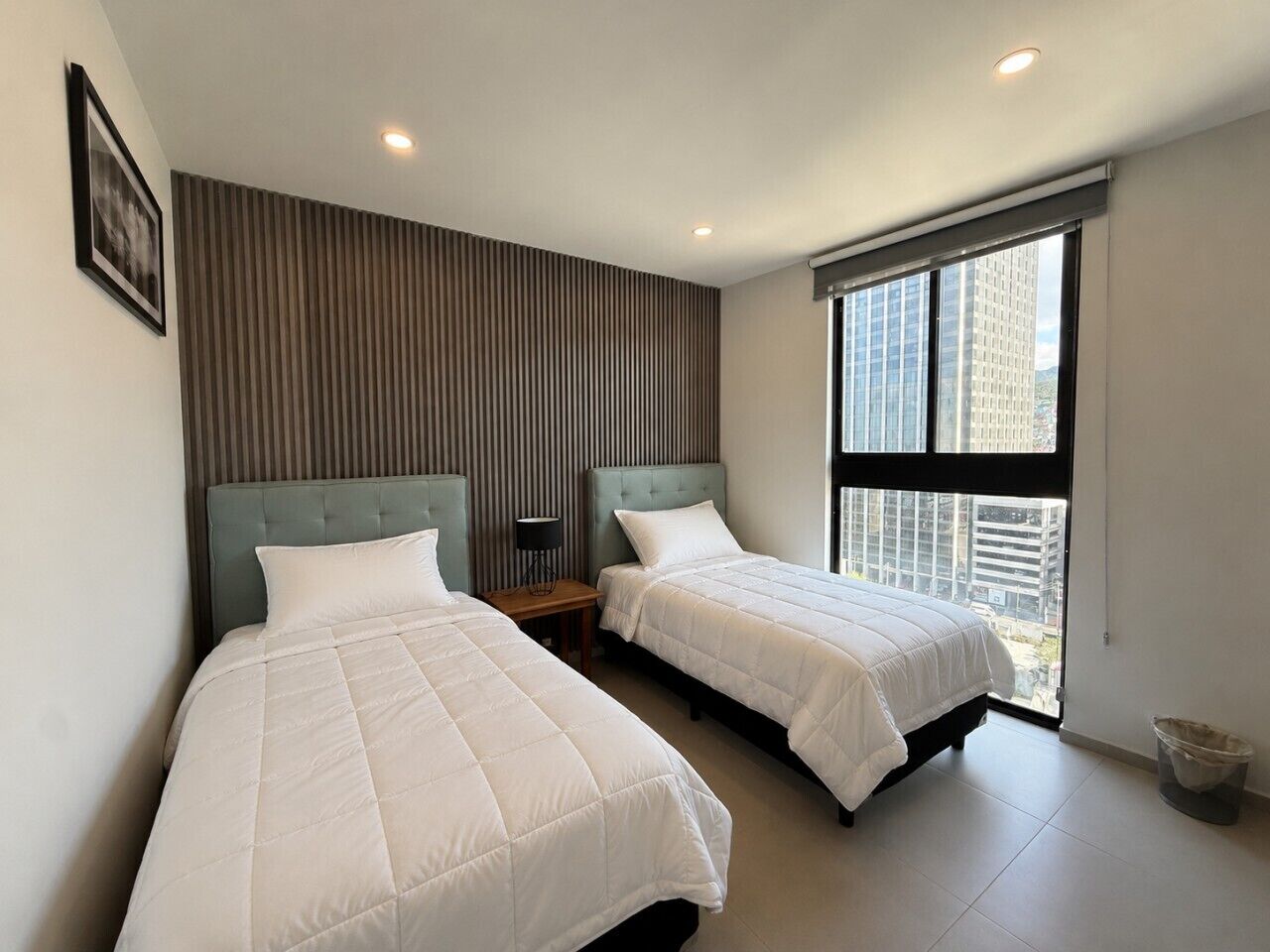 A modern hotel room with two beds, a large window, and a city view.