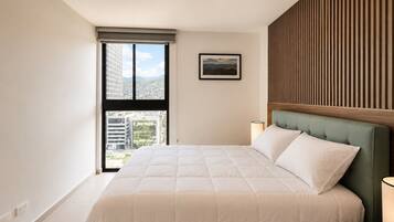 A bedroom with a large bed, a window with a view of buildings, a framed picture on the wall, and a wooden panel design on the wall.