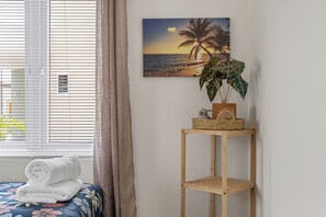 A room with a bed, a window with blinds, a wall-mounted shelf with a plant, and a painting of a beach scene. - Casa Blanca: 4-person vacation bungalow with shared pool (Willemstad)