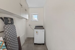 A laundry room with a washing machine, a drying rack, and a small window. - Casa Blanca: 4-person vacation bungalow with shared pool (Willemstad)