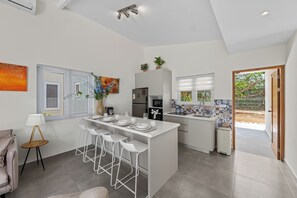 A modern kitchen with white bar stools, a central island, and a dining area. - 4-person vacation bungalow with shared pool (Willemstad)