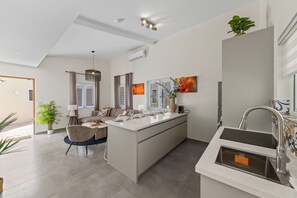 A modern kitchen with a central island, a dining area with a chair and table, and a view of the outdoors. - Casa Blanca: 4-person vacation bungalow with shared pool (Willemstad)