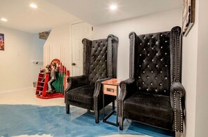 Une pièce comprenant deux fauteuils noirs à revêtement capitonné et aux bords cloutés, une petite table d’appoint en bois et une échelle rouge sur laquelle est posée une figurine.