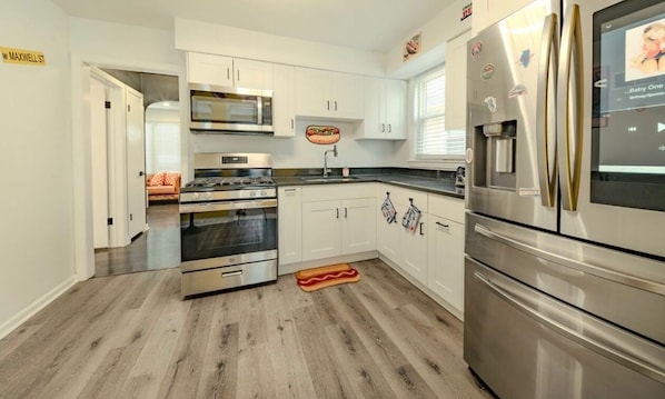 Une cuisine moderne dotée d’appareils électroménagers en acier inoxydable, de meubles blancs et d’un plancher en bois.