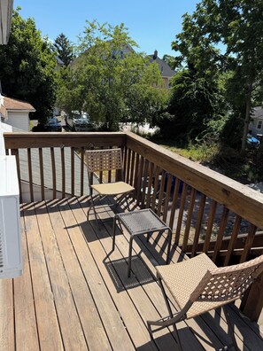 Une terrasse en bois avec deux fauteuils en osier et une petite table, le tout entouré d’une balustrade en bois.