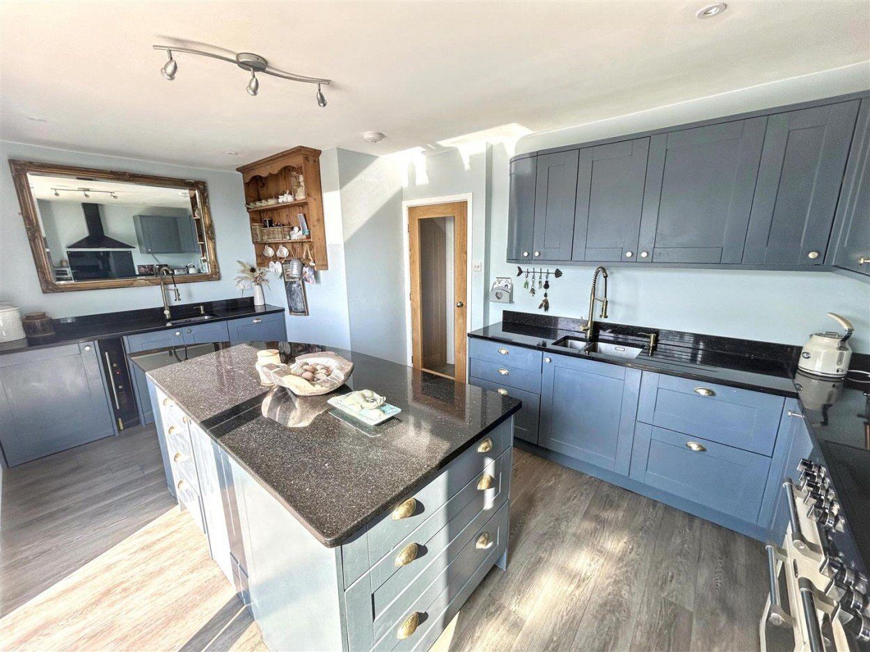 A modern kitchen with a central island, blue cabinets, and a stainless steel range hood.