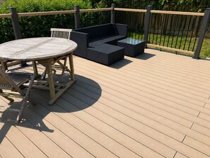 A deck with a round wooden table and two dark-colored sofas. - Portscatho Sea View House with Private Hot Tub. Opposite Porthcurnick Beach (Portscatho, Cornwall)