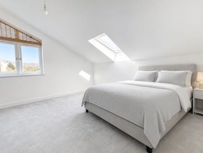 Ein Schlafzimmer mit einem Bett, einem Nachttisch, einer Lampe, einem Fenster und einem Oberlicht.