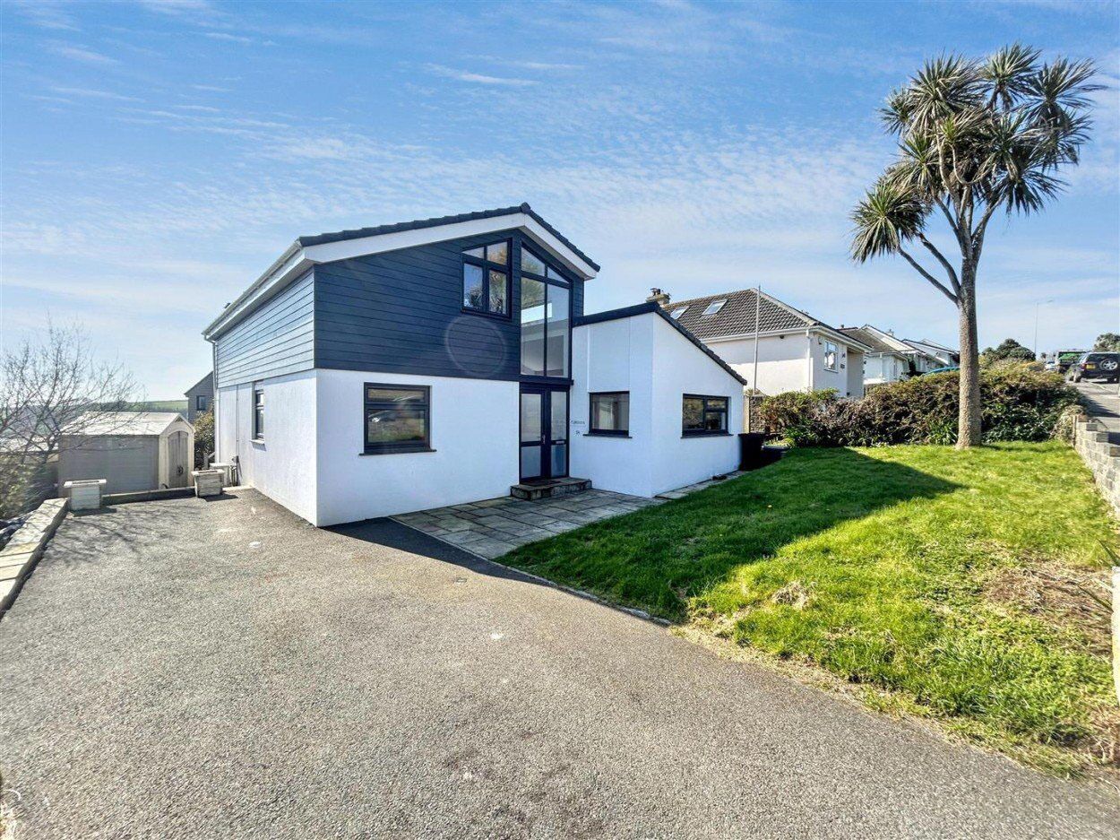 Une maison moderne à deux étages, avec une allée menant à la porte d’entrée, un petit jardin devant et un palmier.