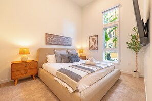 Un dormitorio con cama, lámparas de noche, mesita de noche, ventana con vistas y una planta en maceta.