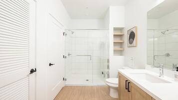 Een moderne badkamer met een douchecabine van glas, een wit toilet en een houten wastafelmeubel met een grote spiegel.