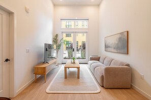 A modern living room with a sofa, a coffee table, a TV, and a large window.