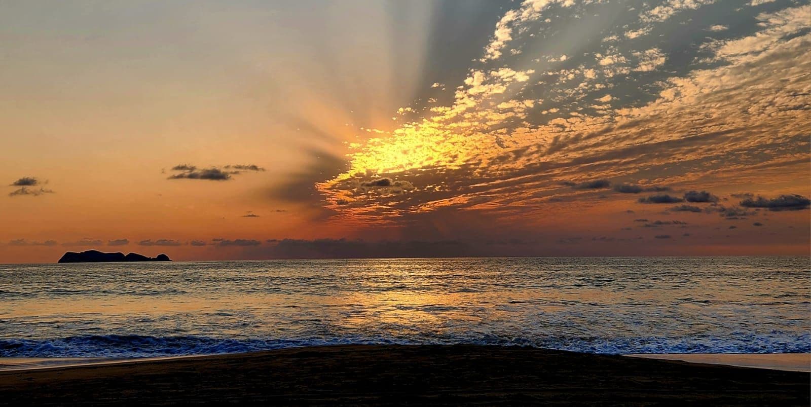 A sunset over the ocean with a silhouette of land in the distance.