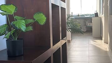 A hallway with a wooden bench, a potted plant, and a window with sheer curtains.