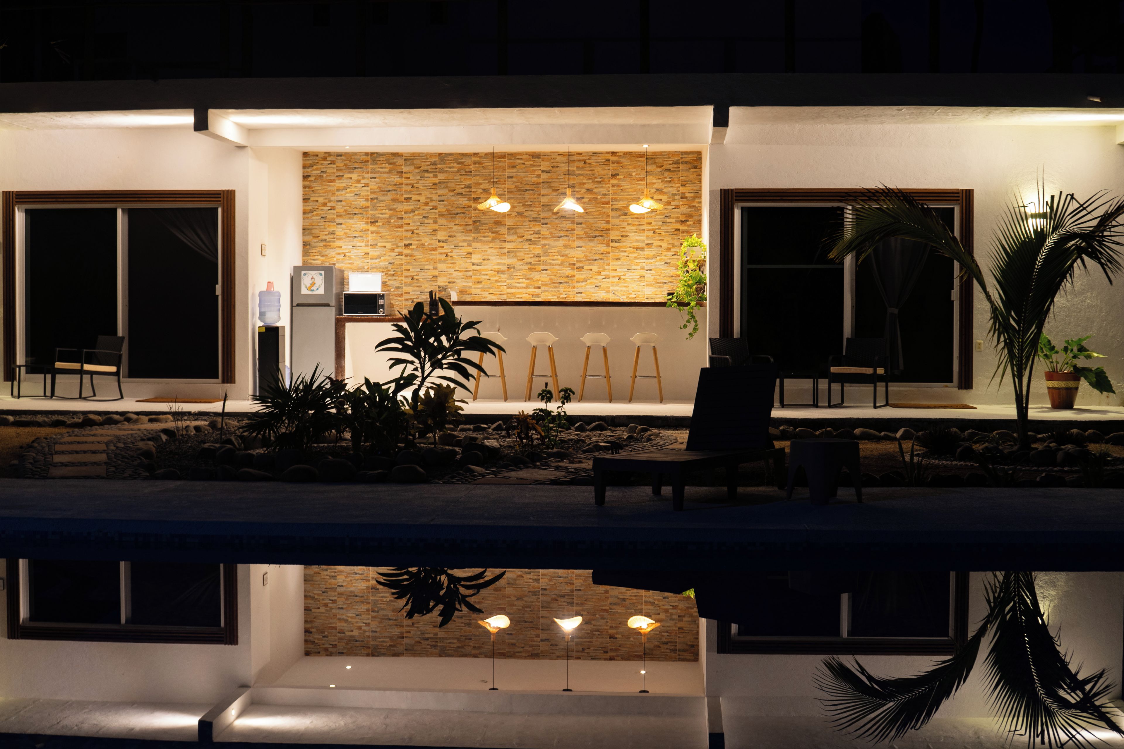 A modern outdoor seating area with a pool, stone wall, and potted plants.