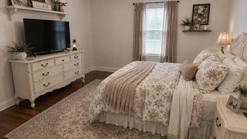 A bedroom with a bed, dresser, television, and a ceiling fan.