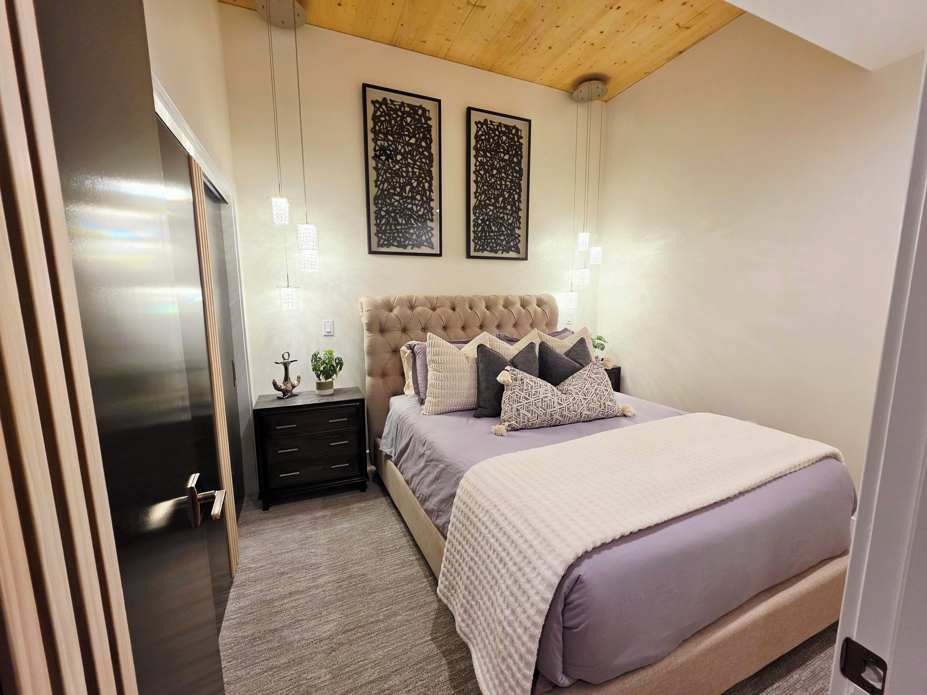 Een slaapkamer met een gestoffeerd hoofdeinde, een bed met meerdere kussens, nachtkastjes en wandlampen.