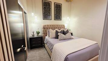 Een slaapkamer met een gestoffeerd hoofdeinde, een bed met meerdere kussens, nachtkastjes en wandlampen.