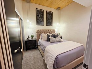 Une chambre à coucher avec une tête de lit capitonnée, un lit agrémenté de plusieurs coussins, des tables de chevet et des lampes fixées au mur.