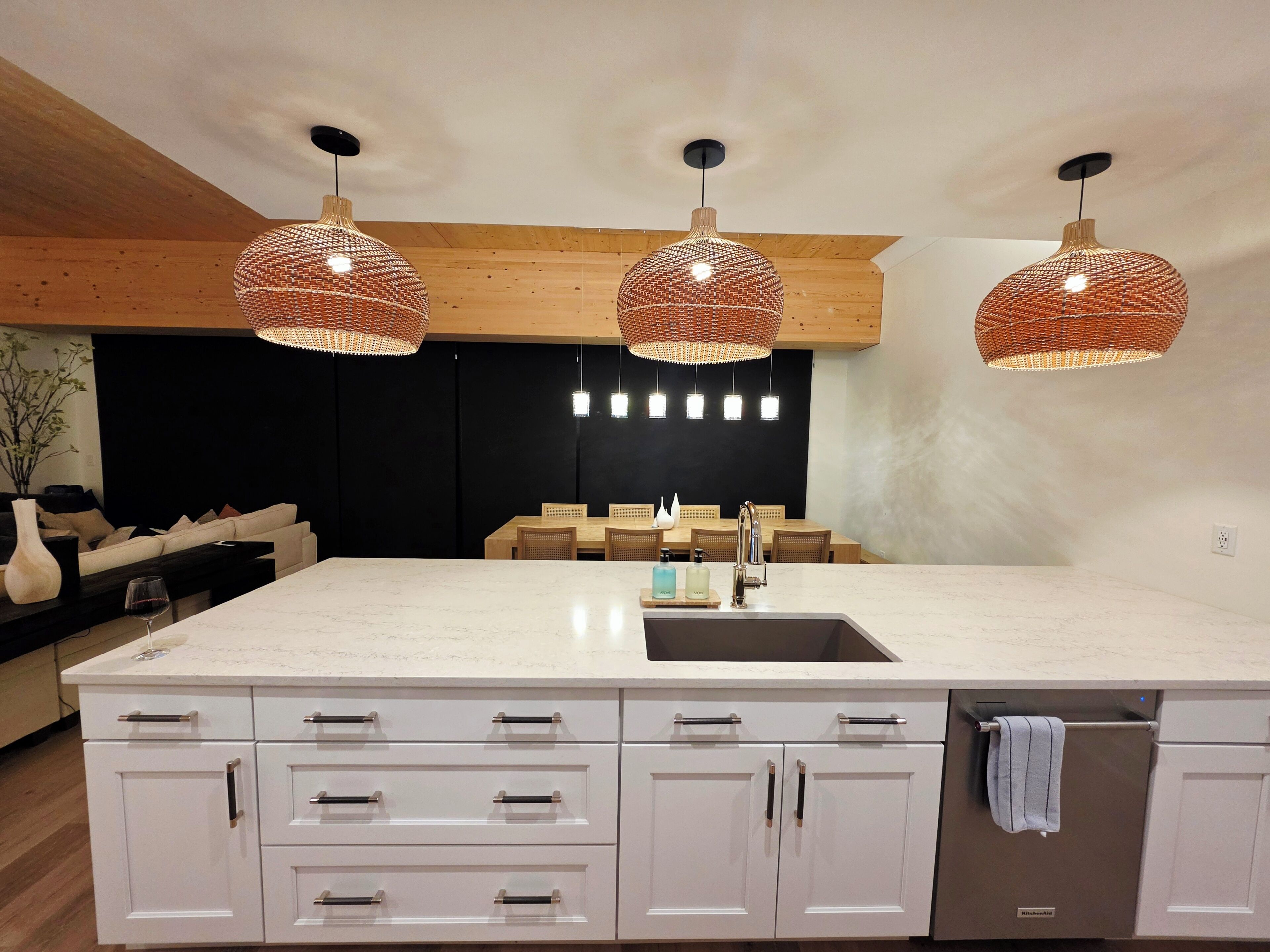 Een moderne keuken met een groot eiland, witte kasten en drie gevlochten hanglampen.