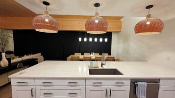 Een moderne keuken met een groot eiland, witte kasten en drie gevlochten hanglampen.