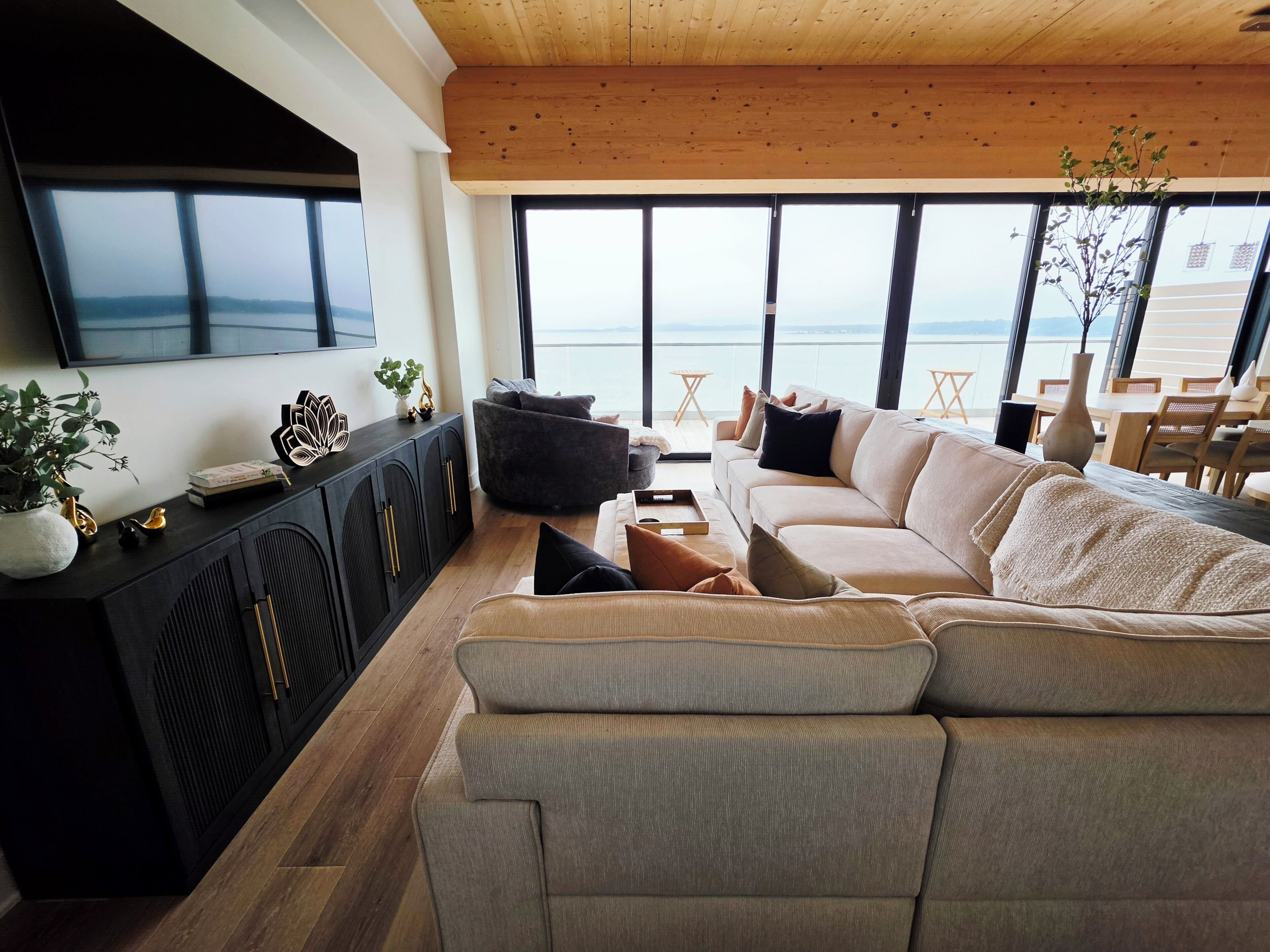 Un salón moderno con un sofá grande, un televisor de pantalla plana en la pared y vistas al mar a través de amplios ventanales.