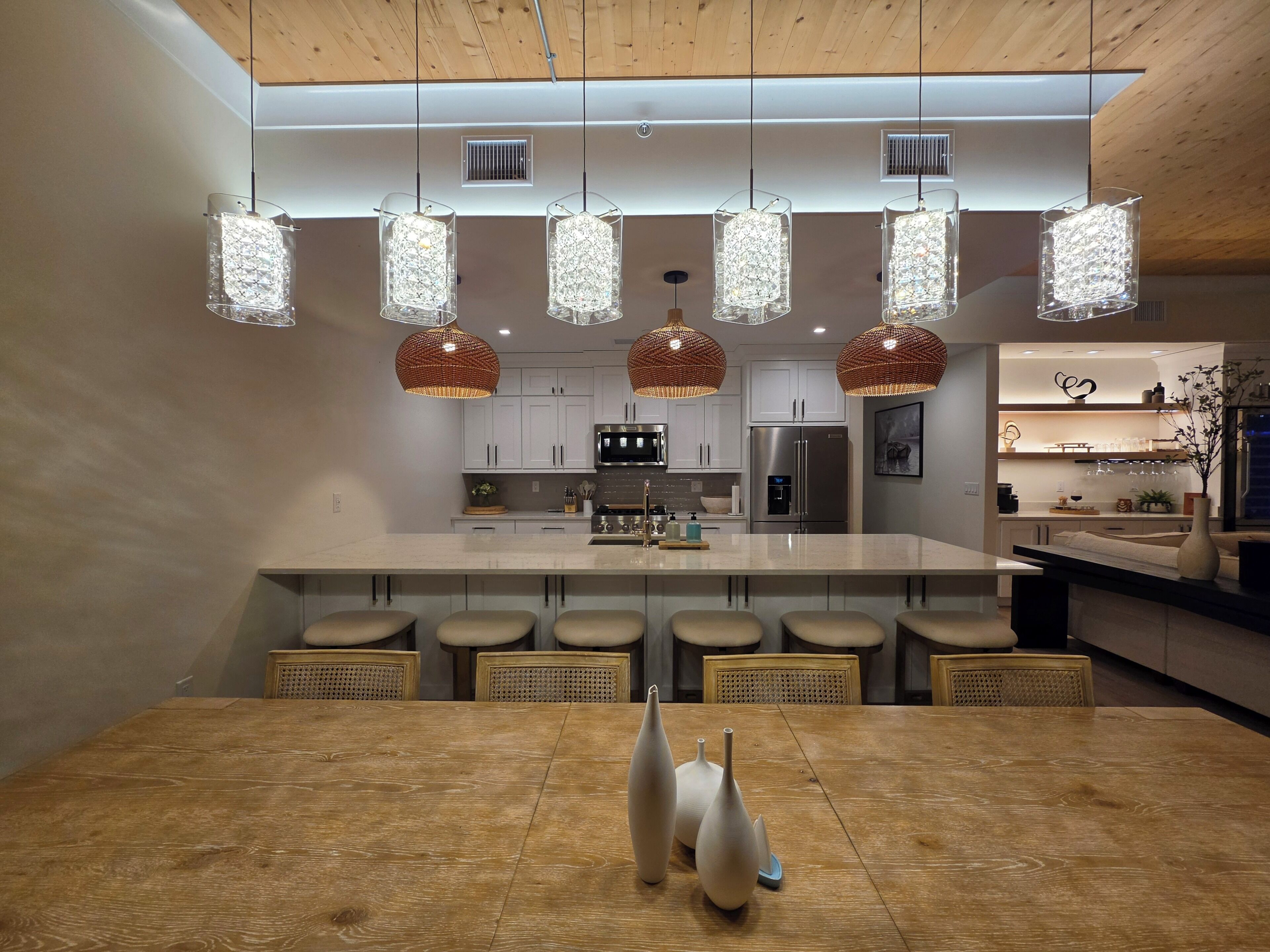 A modern kitchen with a central island, pendant lights, and a dining area with a wooden table.