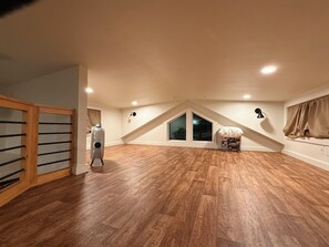 An attic room with wooden flooring, a fan, a window, and a staircase.