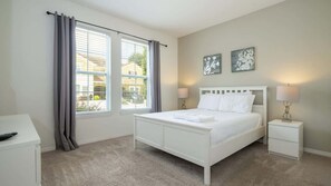 Ein Schlafzimmer mit einem Bett, Nachttischen, Vorhängen an einem Fenster und zwei Wandlampen.
