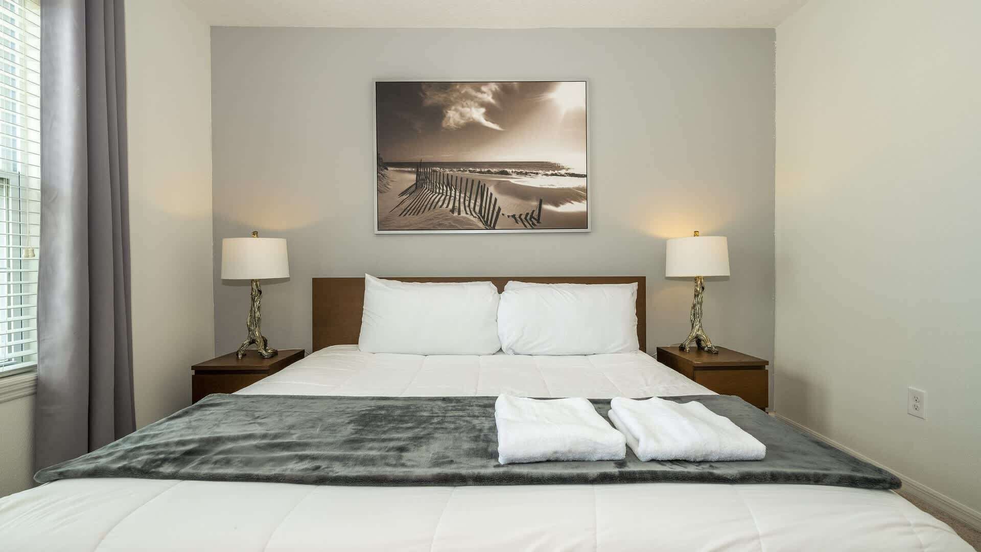 Een hotelkamer met een bed, twee nachtkastjes, een lamp, een schilderij en een raam met gordijnen.