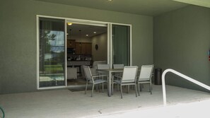 Ein Balkon mit Tisch und Stühlen, eine Schiebetür zu einer Küche und ein Feuerlöscher an der Wand.