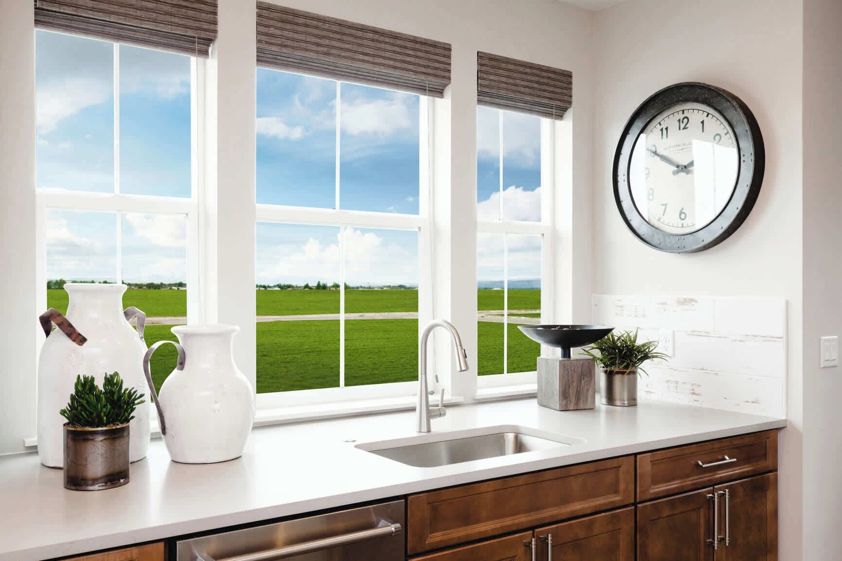 A kitchen with a large window, a sink, cabinets, a clock, and decorative items.