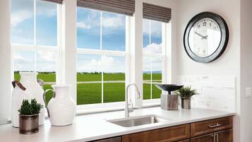 A kitchen with a large window, a sink, cabinets, a clock, and decorative items.