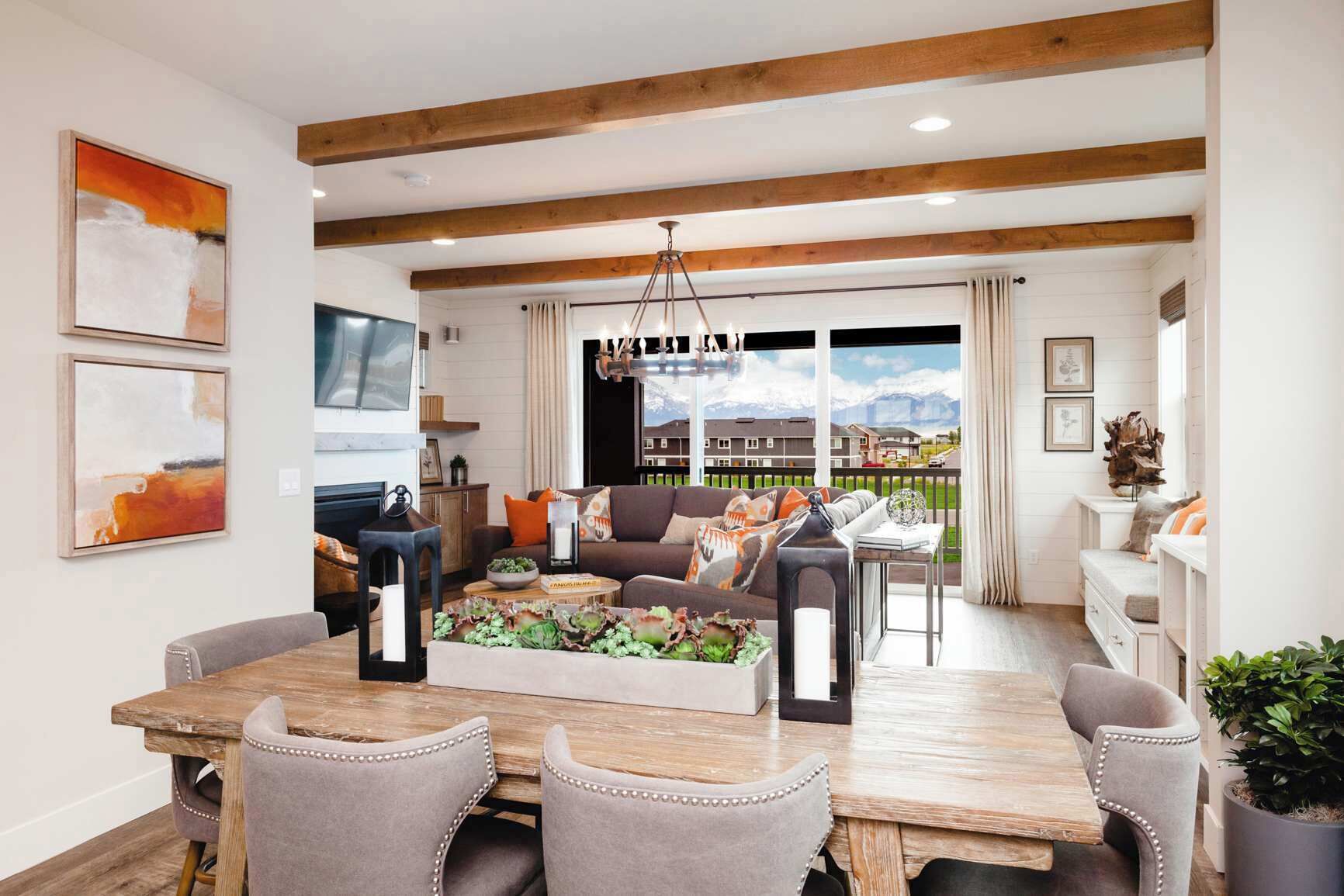 A spacious living room with a dining area, wooden beams on the ceiling, a large window with a view, and a fireplace.