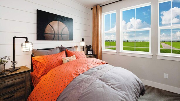 A bedroom with a bed, a nightstand, a lamp, a painting, and a view of a green field through large windows. - Iconic Big Sky Getaway | Epic Yellowstone Retreat! (Belgrade)